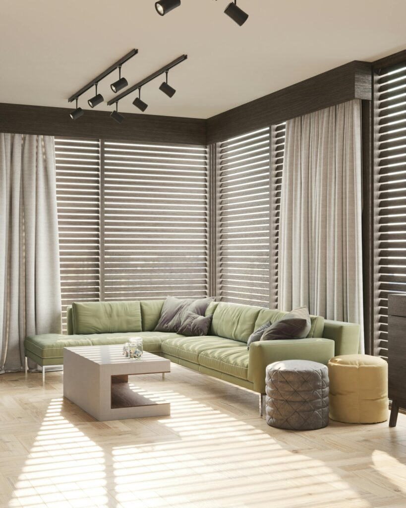 A modern living room with a green sofa, poufs, and sleek wooden blinds allowing natural light to filter through.